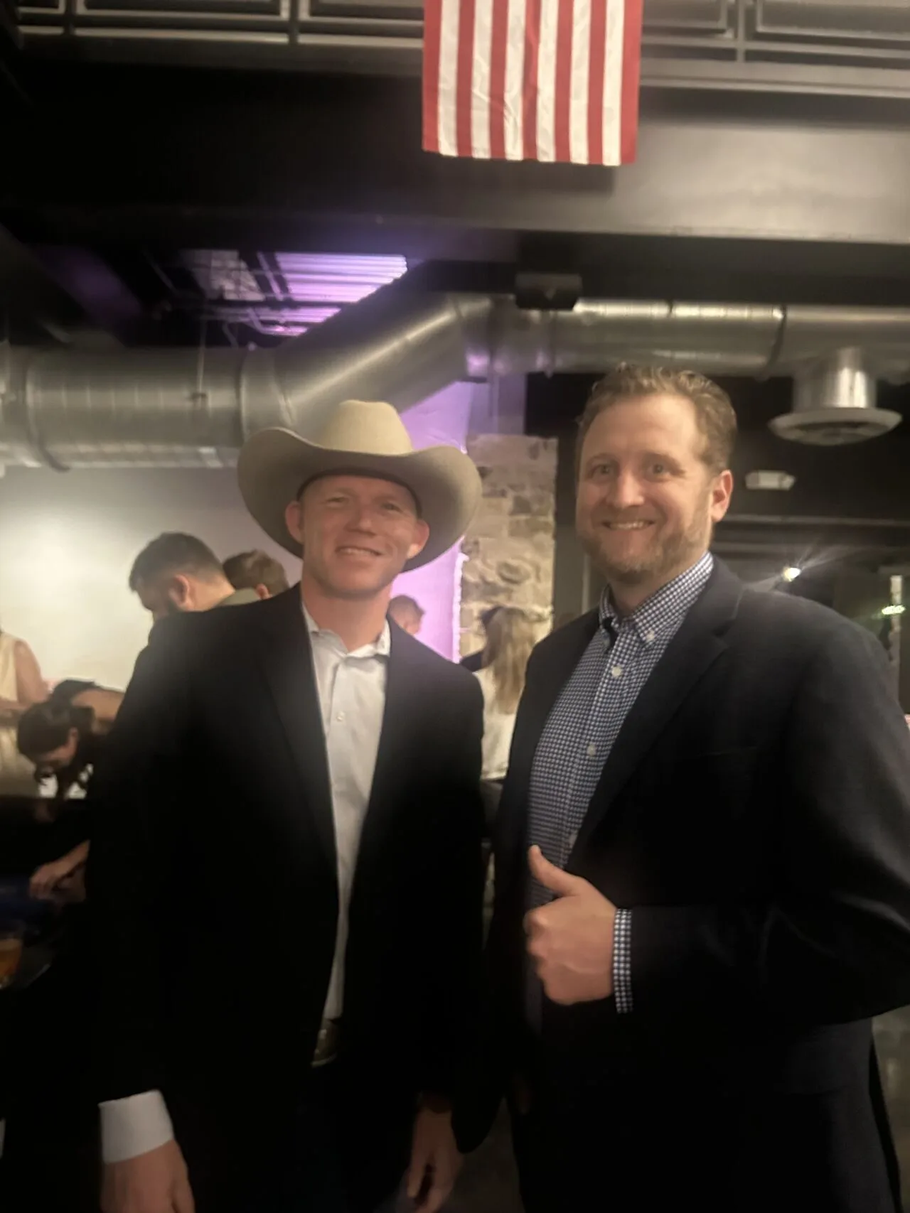 Two men in suits, one wearing a cowboy hat, standing together and smiling.