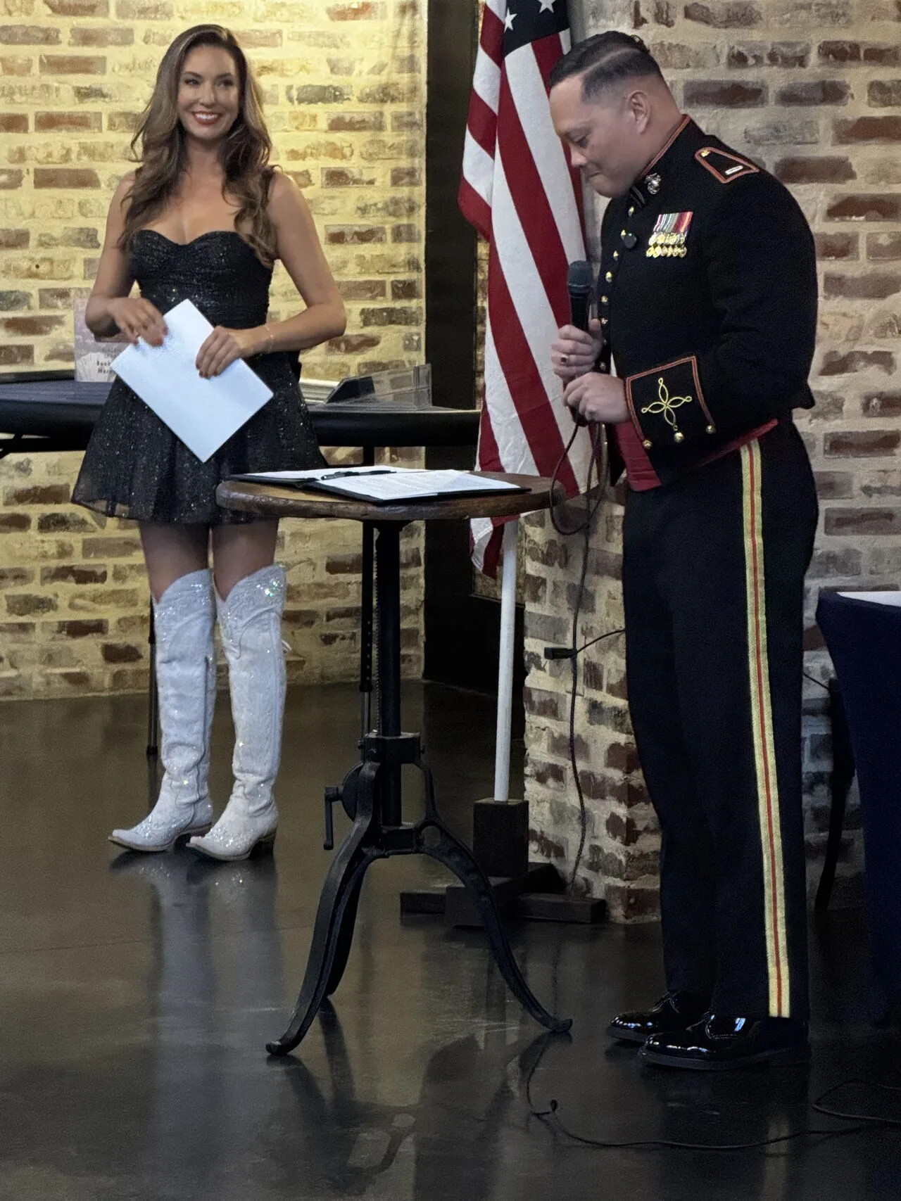 Man in military uniform speaks into a microphone while a woman stands beside him.
