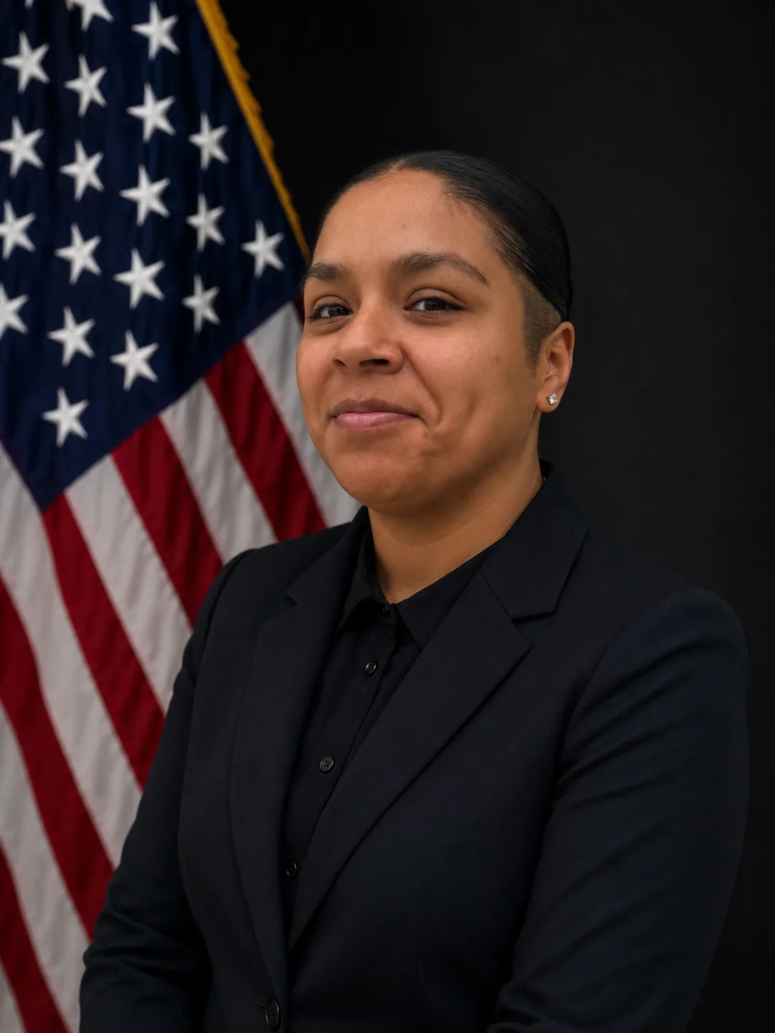 Woman in a black suit standing in front of an American flag.
