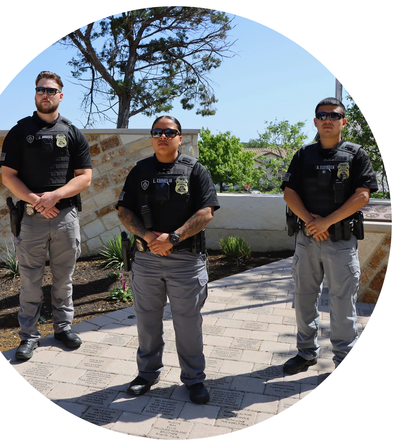 Three police officers stand on a brick walkway, wearing sunglasses and uniforms with badges.