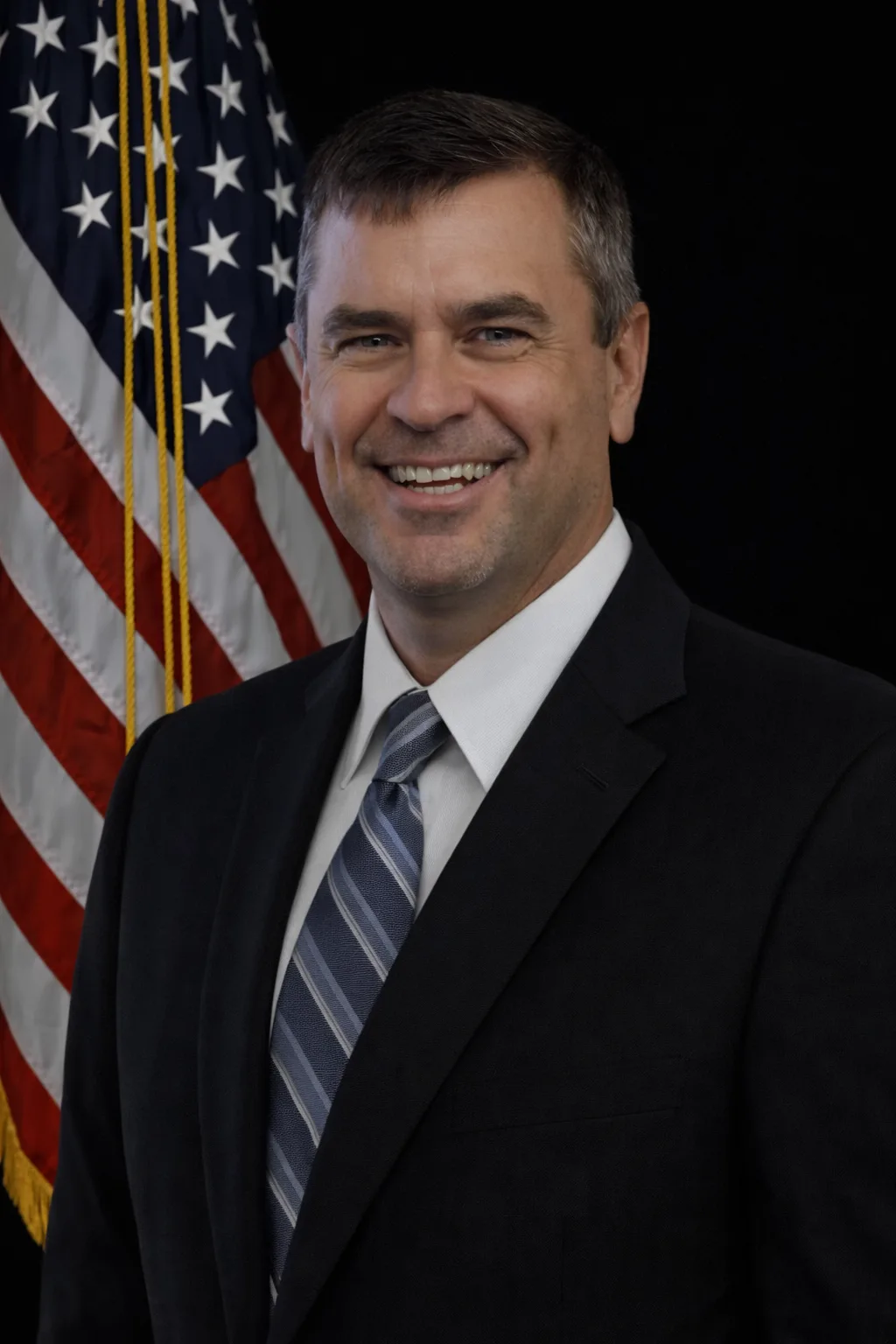 Man in a suit standing in front of an American flag.