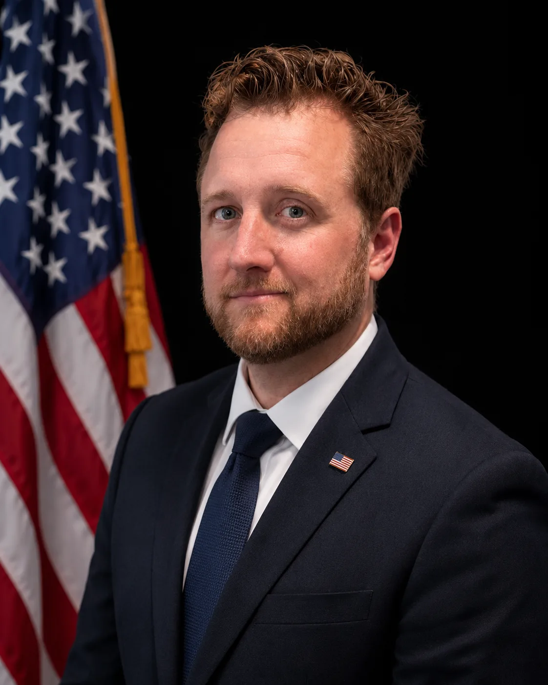 Man in a suit standing in front of an American flag.