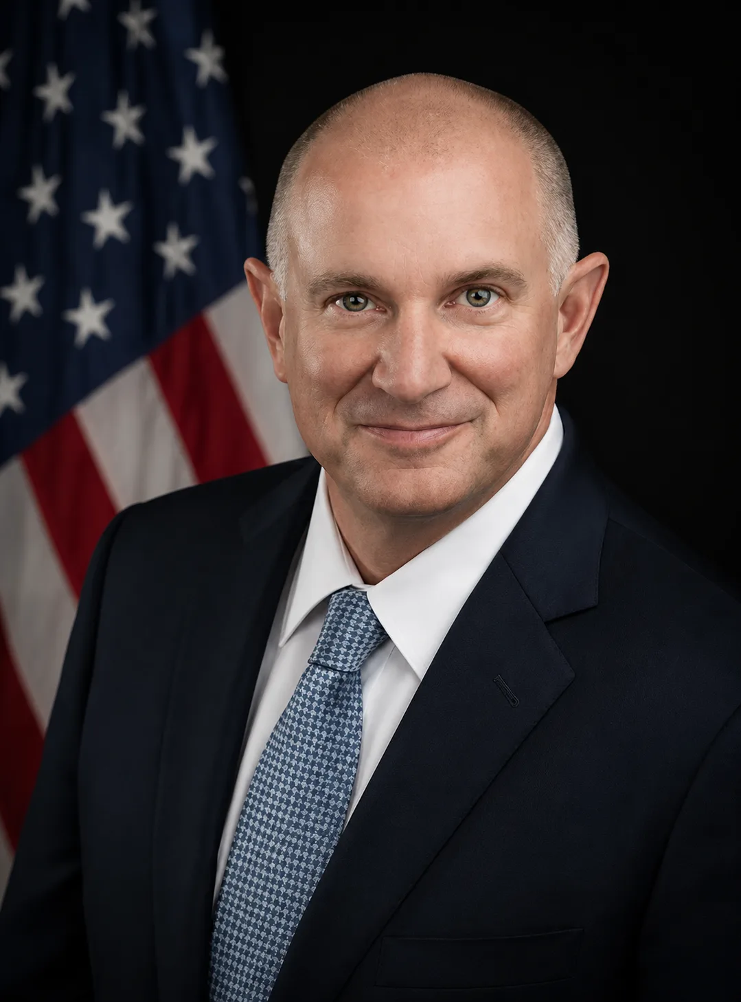 Man in a suit and tie standing in front of an American flag.