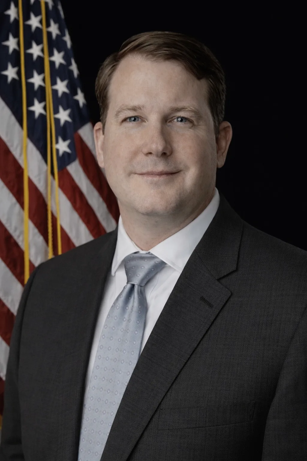 Man in a suit standing in front of an American flag.