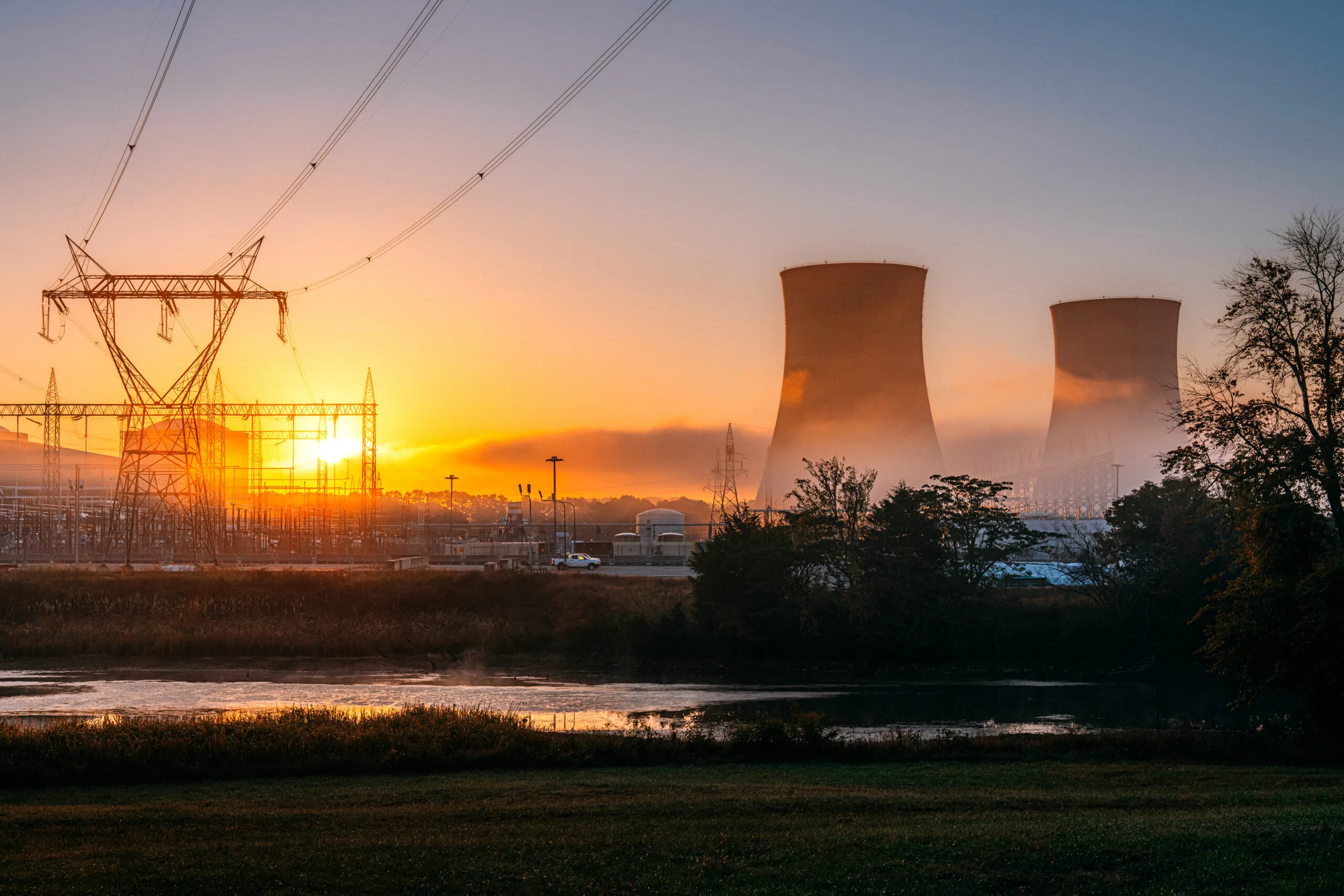 A nuclear power plant at sunrise with cooling towers and power lines.